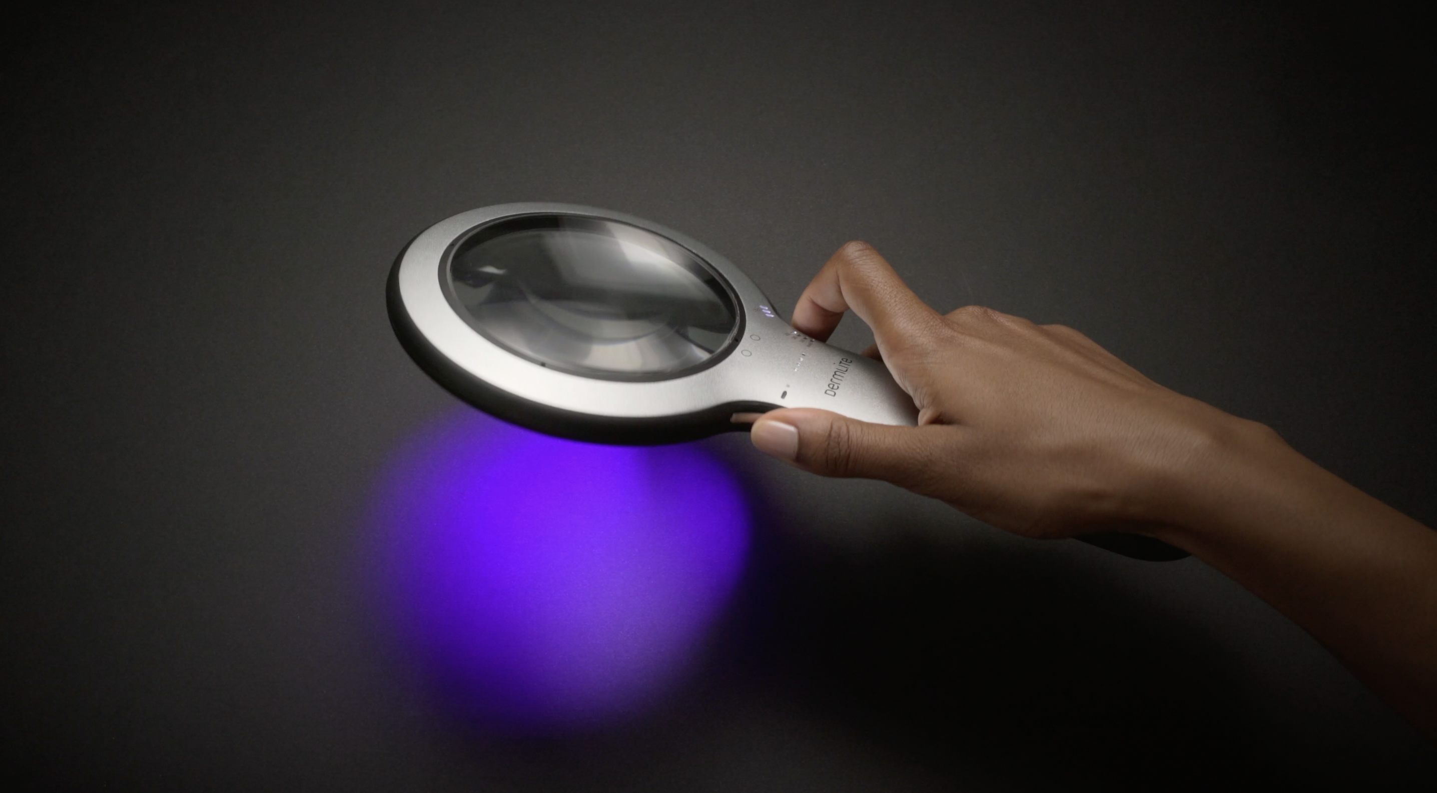 Hand holding DermLite Lumio 2 dermatoscope with UV light on.