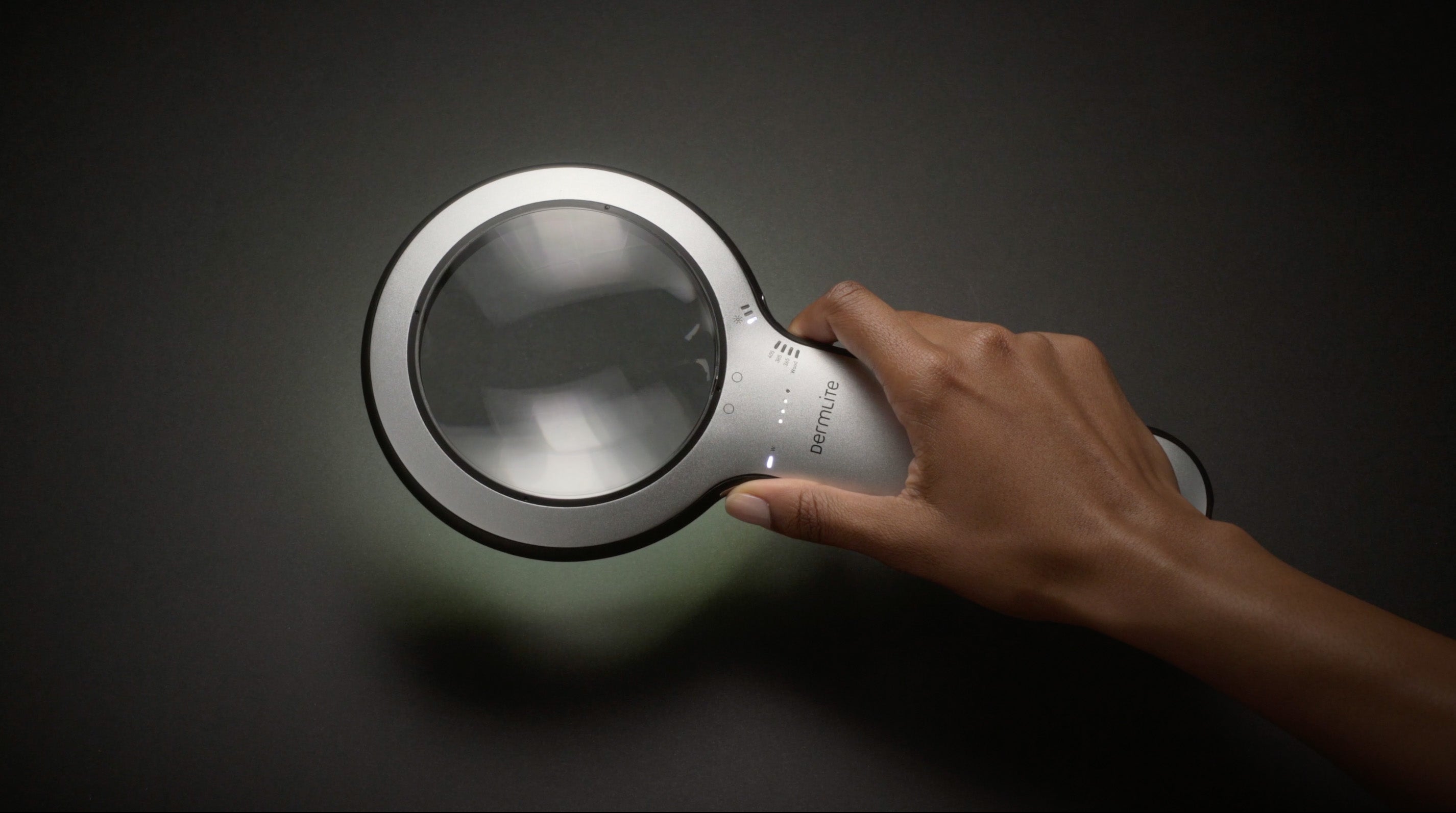 Hand holding DermLite Lumio 2 dermatoscope turned on.