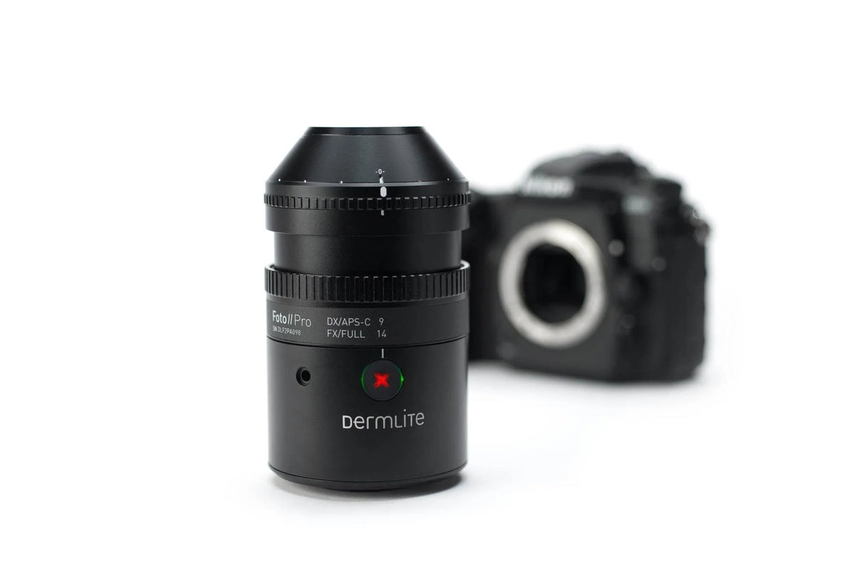 A black Dermlite DVAPS-C 7 full-frame camera lens in sharp focus in the foreground, with a blurred black camera body in the background on a clean white studio backdrop.