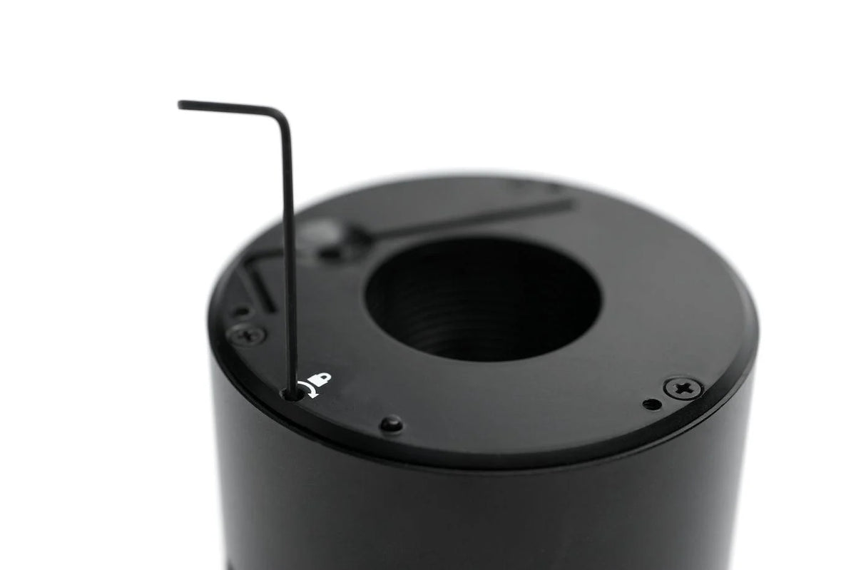 Close-up of a black cylindrical component with a circular opening and a small Allen wrench inserted into a screw hole on top, photographed against a white background.