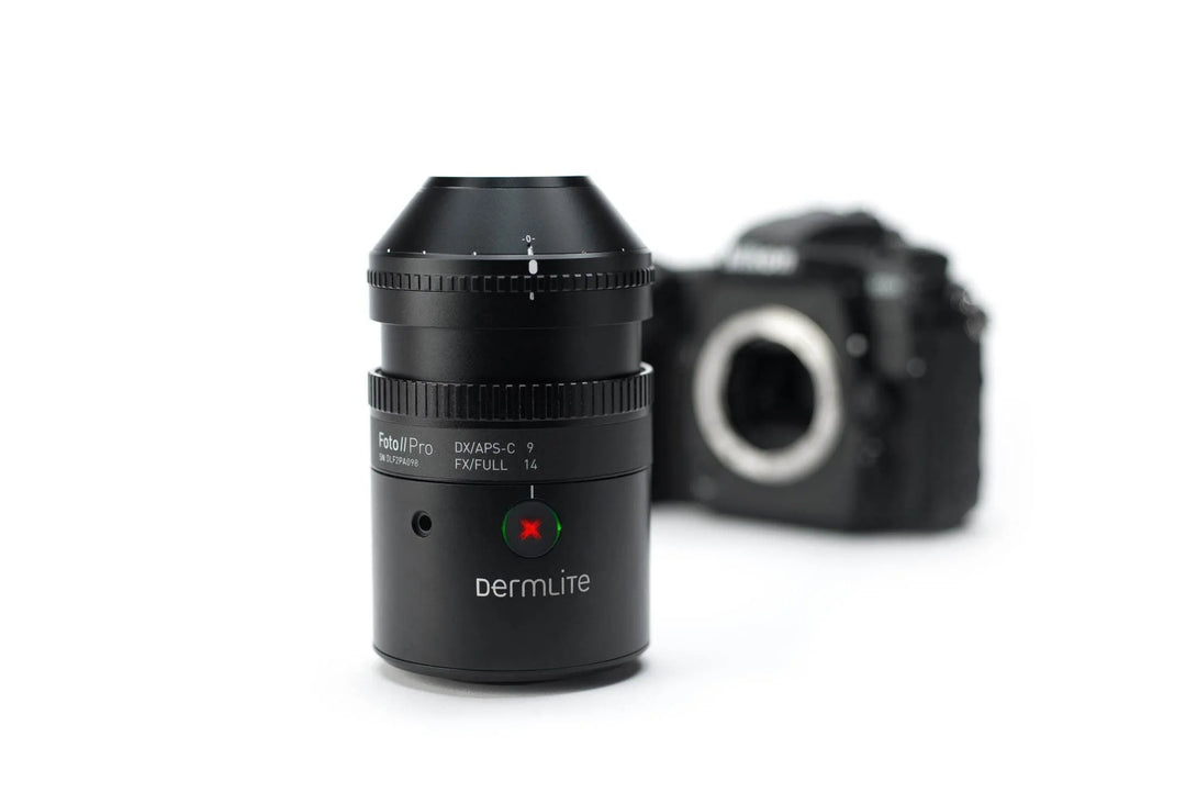 A black Dermlite DVAPS-C 7 full-frame camera lens in sharp focus in the foreground, with a blurred black camera body in the background on a clean white studio backdrop.