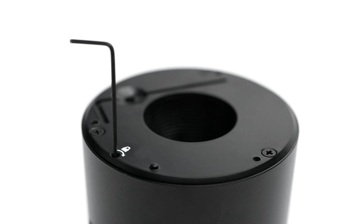 Close-up of a black cylindrical component with a circular opening and a small Allen wrench inserted into a screw hole on top, photographed against a white background.