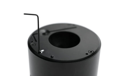 Close-up of a black cylindrical component with a circular opening and a small Allen wrench inserted into a screw hole on top, photographed against a white background.